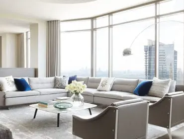 Living room with large sectional sofa, marble coffee table, and city view through floor-to-ceiling