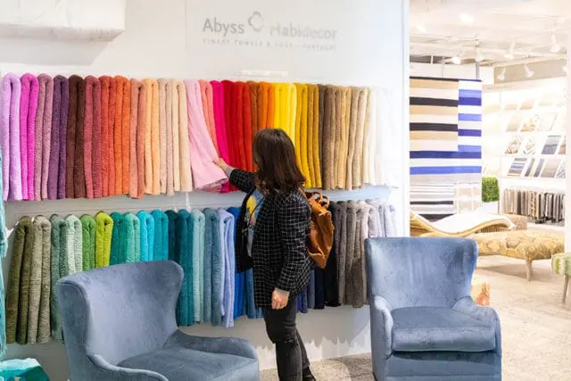 Woman browsing colorful towels displayed on a wall in a store with blue chairs.