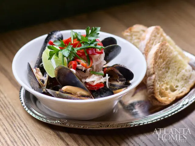 Bowl of mussels with lime, red peppers, and parsley, served with toast on a silver platter.