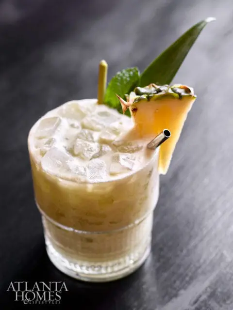 Cocktail with ice, pineapple wedge, mint, and metal straw in glass