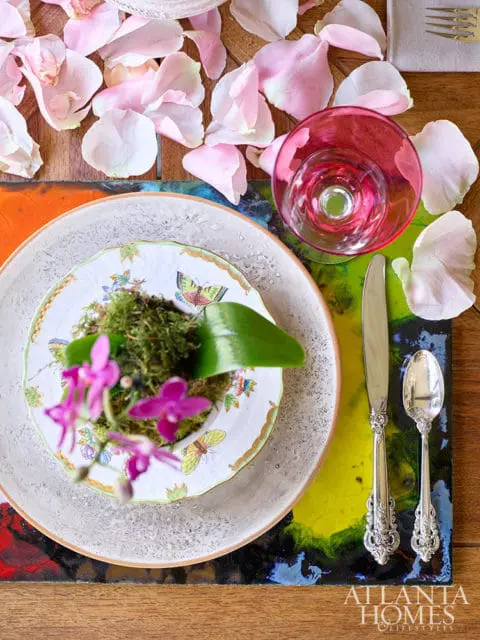 Table setting with pink orchid, moss, butterfly plate, pink glass, and ornate silverware on