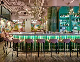 Bar with pink stools, a white counter, and a green tiled backsplash. Mural art on the wall.