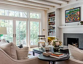 Living room with large glass doors, built-in bookshelves, fireplace, and neutral-toned furniture. A colorful painting hangs above the mantel.