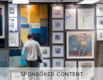 Man looking at framed artwork on a gallery wall.