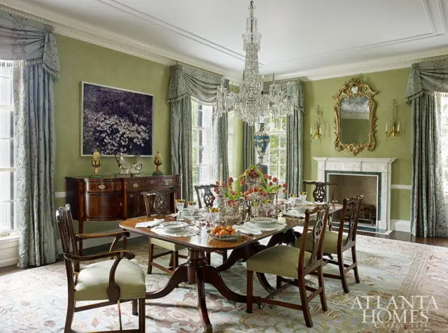 Dining room with green walls, crystal chandelier, dark wood table set for dinner, and ornate mirror