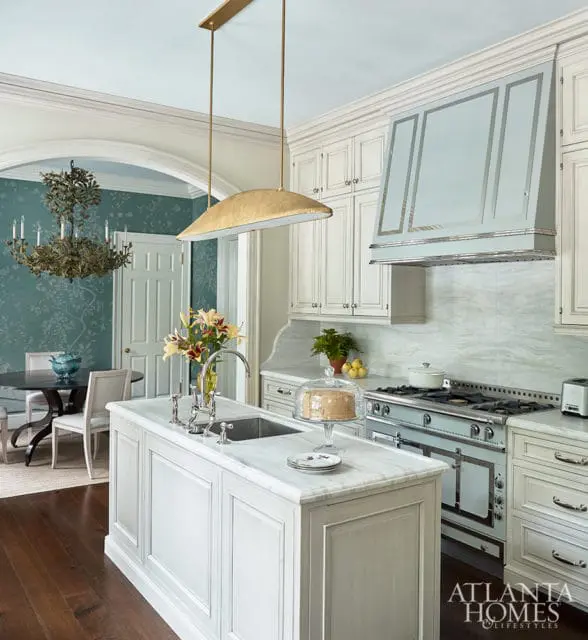 White kitchen island with marble countertop and sink, gold pendant light, and range with light blue