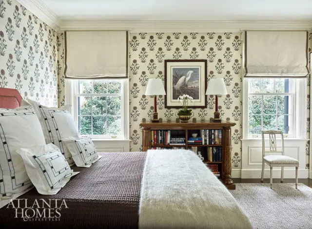 Bedroom with floral wallpaper, bed with white pillows, and a wooden bookshelf filled with books.
