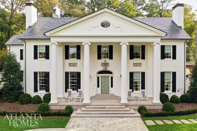White neoclassical house with large columns, black shutters, and a green front door.