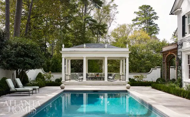 Poolside gazebo with seating, lounge chairs, and manicured hedges.