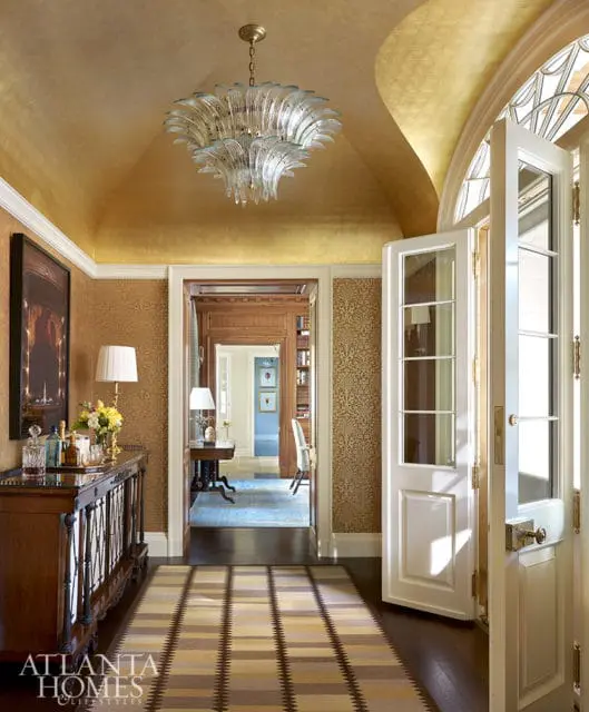 Hallway with gold leaf ceiling, glass chandelier, and patterned wallpaper.