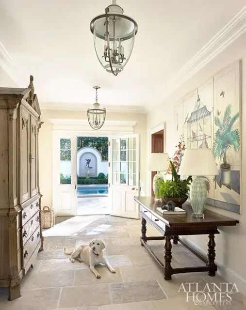 Hallway with stone floor, antique cabinet, console table, and artwork. Dog lies on floor.