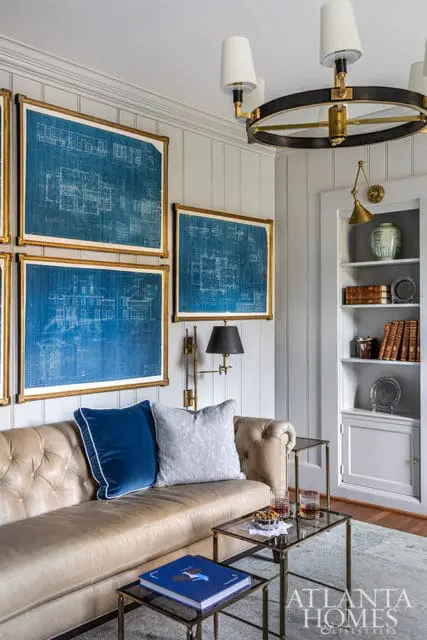 Living room with tufted leather sofa, blue and gray pillows, framed blueprints, and built-in