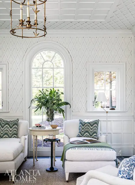 White living room with arched window, diamond patterned wallpaper, and upholstered chairs.