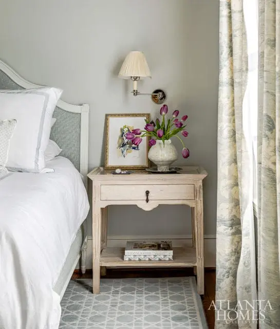 Bedroom with upholstered headboard, bedside table with tulips, and patterned curtains.