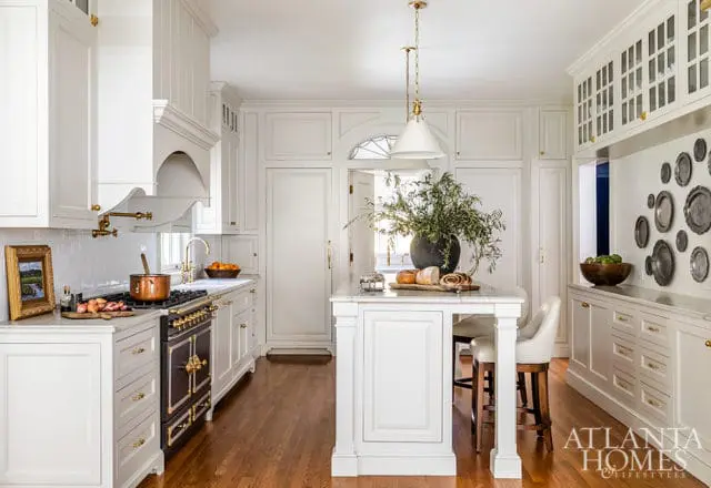 White kitchen with marble island, brass hardware, dark range, and pendant lights.