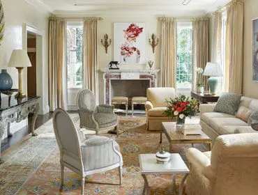 Living room with cream sofa, patterned rug, ornate console table, and floral artwork above