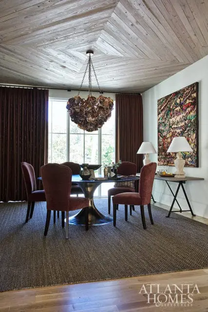 Dining room with dark red chairs, metal pedestal table, and wood plank ceiling.