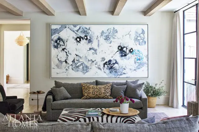 Living room with gray sofa, abstract floral art, zebra ottoman, and exposed wood beams.