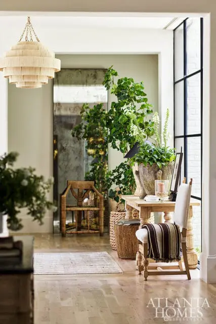 Entryway with tiered chandelier, tall antique mirror, wooden chair, and console table with plants.
