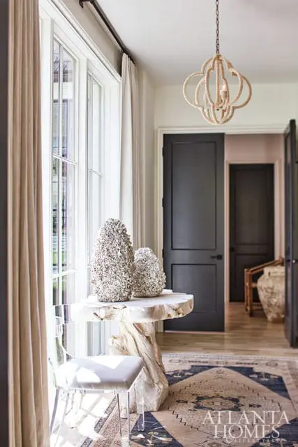 Entryway with light wood table, textured decor, acrylic chair, and dark doors.