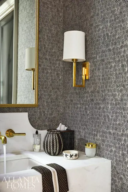 Bathroom with black and white speckled wallpaper, brass sconce, and marble vanity.
