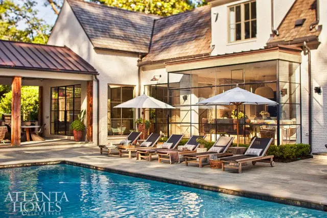 Luxury home with white brick exterior, large glass windows, and pool patio with lounge chairs.