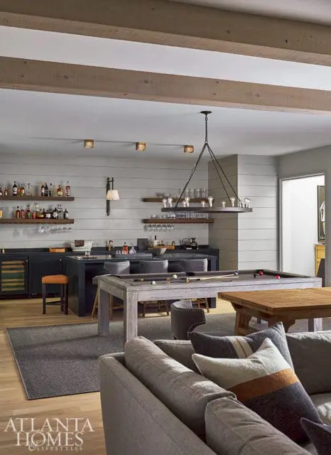Gray pool table and bar area with wood beams and shiplap walls.