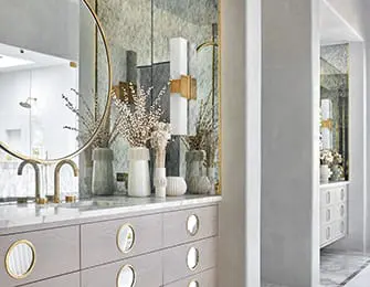 Bathroom vanity with light wood drawers, brass hardware, marble countertop, and round mirror.