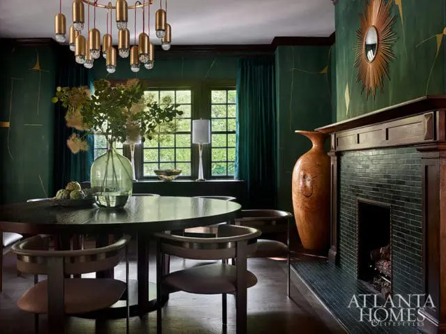 Dark wood dining table and chairs in a room with emerald green walls, a fireplace, and a gold