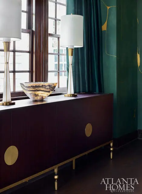 Dark wood sideboard with brass hardware, two white lamps, and a stone bowl.