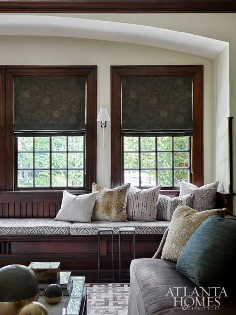 Dark wood built-in bench with patterned cushions and pillows, flanked by two windows with dark