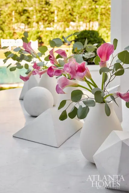 Pink calla lilies and eucalyptus in white vases with geometric sculptures on marble table