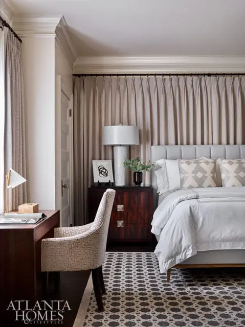Bedroom with gray upholstered headboard, white bedding, patterned accent pillows, and a dark wood