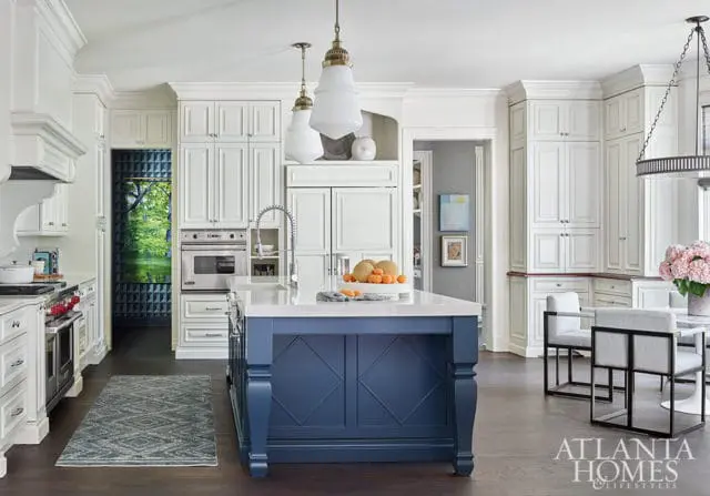 White kitchen with blue island, marble countertops, and stainless steel appliances.
