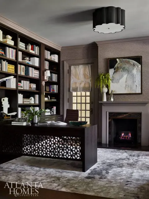 Dark wood desk with geometric pattern, built-in bookshelves, fireplace, and abstract horse painting.
