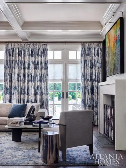 Living room with coffered ceiling, blue patterned curtains, abstract art, and fireplace.