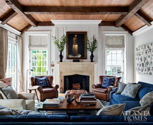 Living room with exposed wood beams, stone fireplace, leather armchairs, and blue sofa.