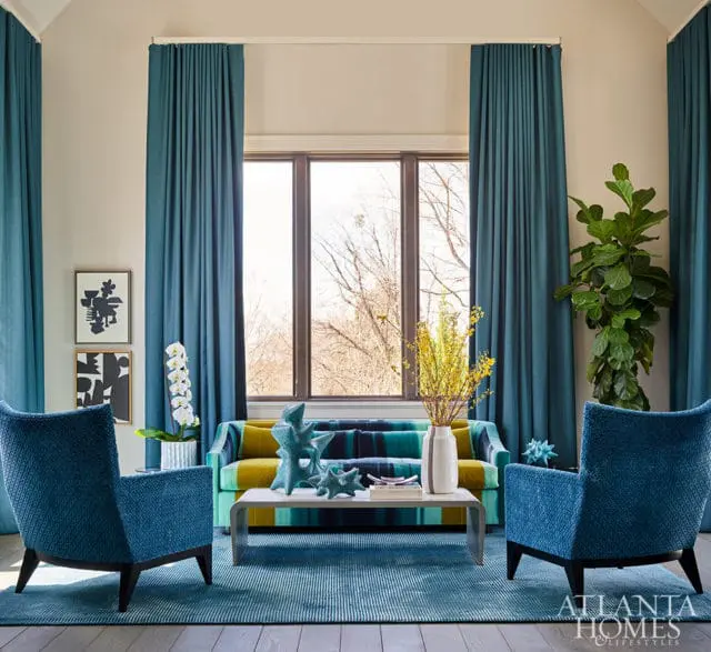 Living room with teal curtains, striped sofa, blue chairs, and abstract art.