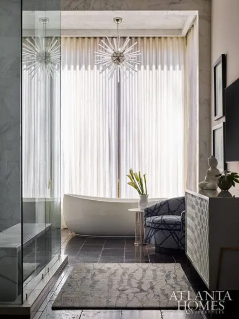Bathroom with freestanding tub, patterned armchair, and starburst chandelier.