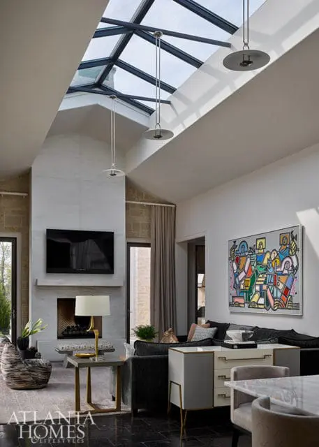 Living room with vaulted ceiling, skylight, marble fireplace, abstract art, and modern furniture.