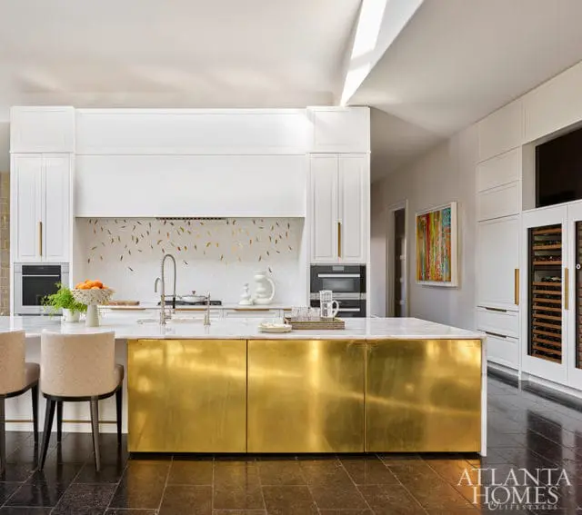 White kitchen with brass island, marble countertop, and gold leaf backsplash