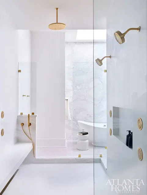 Modern white bathroom with brass showerheads, marble accents, and a freestanding tub.