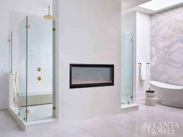 Modern bathroom with glass shower, freestanding tub, fireplace, and marble accent wall.