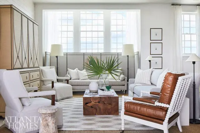 Living room with neutral sofas, leather armchair, wood coffee table, and large windows.