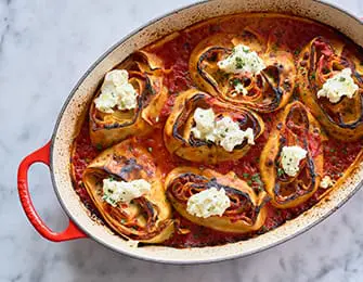 Rolled lasagna with ricotta cheese topping in a red oval baking dish with marinara sauce