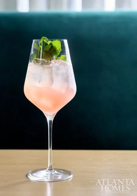Pink cocktail with ice and mint garnish in a stemmed glass