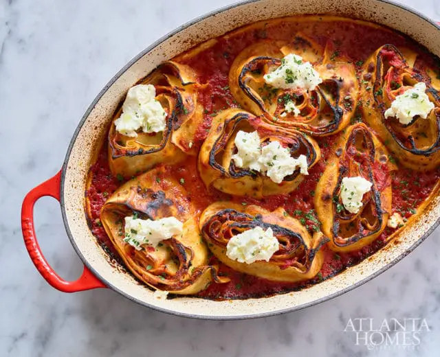 Rolled lasagna with ricotta cheese topping in a red oval baking dish