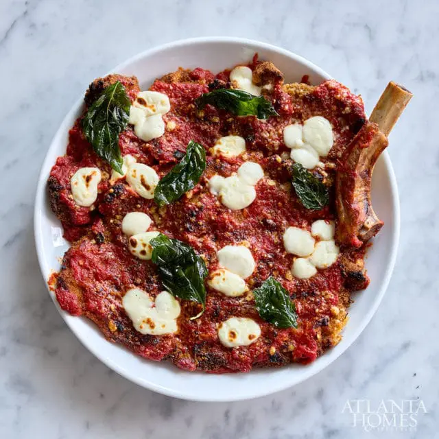 Breaded cutlet with marinara sauce, dollops of mozzarella, and basil leaves, served with a bone-in
