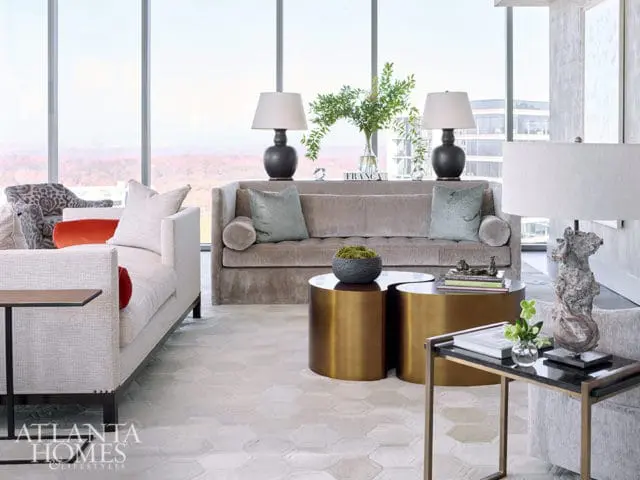 Living room with taupe sofa, gold coffee tables, and large windows overlooking city.