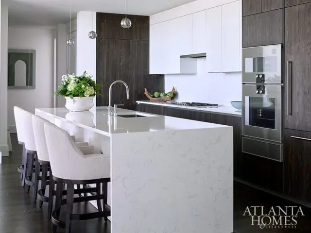 Modern kitchen with white quartz island, dark wood cabinets, and stainless steel appliances.